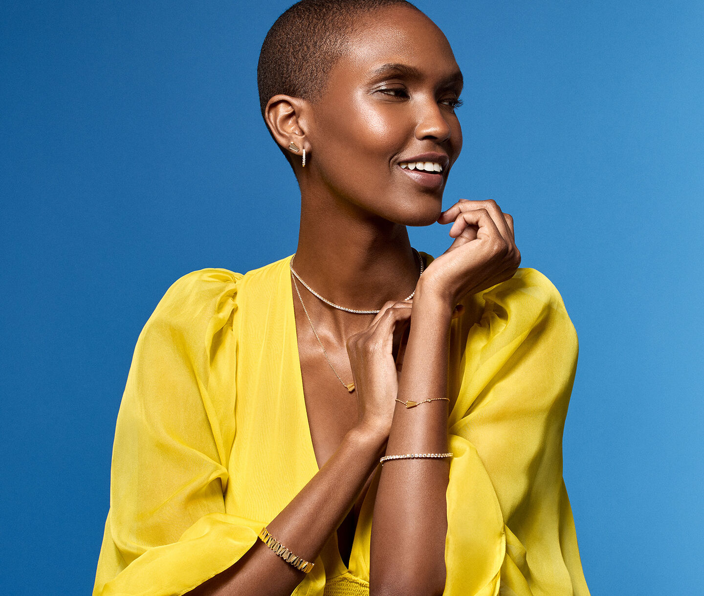 A woman wearing yellow gold jewellery from Birks on a blue background.